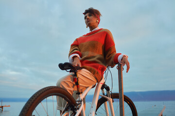 Outdoor portrait of happy african woman admiring sunset over the lake during bike ride