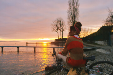 Outdoor portrait of happy african woman admiring sunset over the lake during bike ride