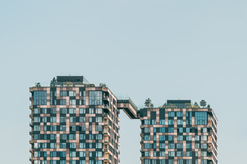 Modern residential twin towers with skybridge and rooftop gardens against clear sky