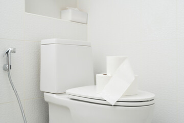 Clean white toilet with tissue paper rolls placed on seat cover in modern bathroom interior hygiene concept