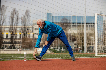 Obraz premium Full length of senior sportsman stretching his legs on stadium during warmup exercises.