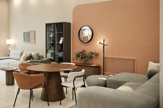 Modern furniture showroom displaying contemporary sofas, armchairs, dining table with chairs, decorative mirror and lighting fixtures arranged in stylish interior setting