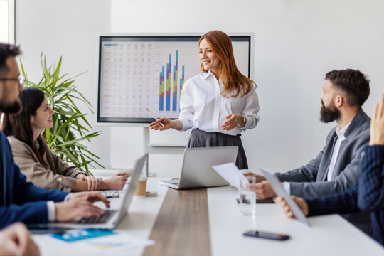 Portrait of female executive standing near conference table at boardroom with her leadership team and explaining financial report.