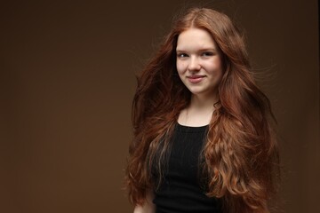 Naklejka premium Portrait of beautiful teenage girl with healthy wavy hair on brown background. Space for text
