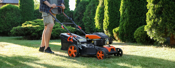 Man cutting green grass with lawn mower in garden