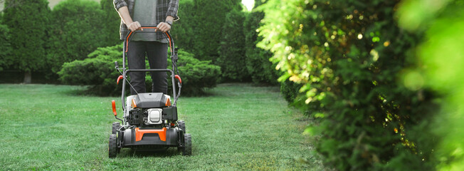Man cutting green grass with lawn mower in garden, closeup