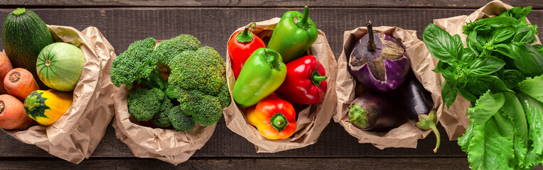 Collage of eco friendly and organic vegetables in paper bags on wooden background, wide panorama