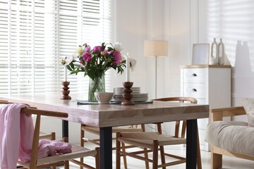Dining table with beautiful flowers and dishware in room. Interior design