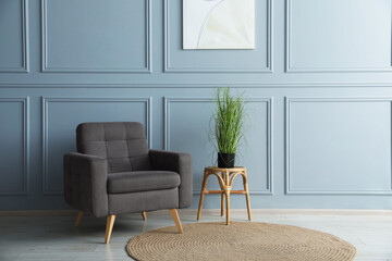 Comfortable armchair and houseplant near light blue wall indoors