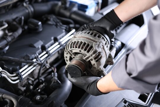 Auto part. Professional mechanic with alternator near open hood of car indoors, closeup