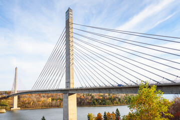 Modern suspension road bridge with tall concrete pylons spanning a river with forested banks in Maine on sunny autumn day