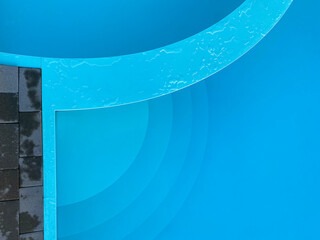 Minimal close-up of a swimming pool with curved shapes, water texture, and contrasting materials. 