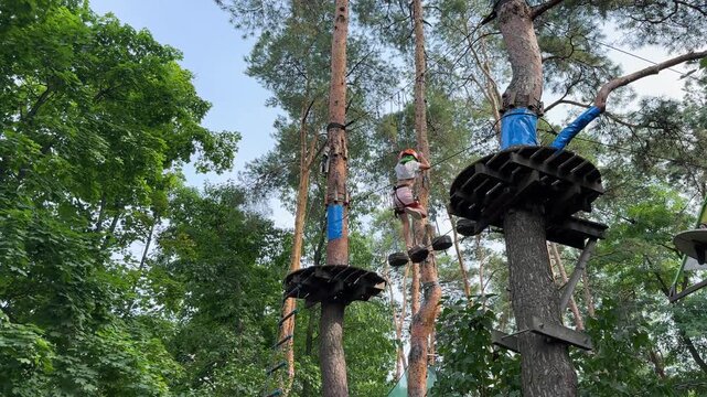 Active lifestyle and outdoor recreation: Girl balancing on a rope bridge and conquering a challenge high-ropes adventure course in a canopy adventure park. Summer vacation activity concept