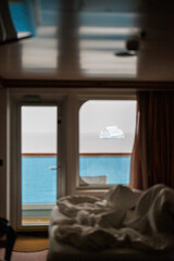 View from a cruise ship cabin showing drifting iceberg in calm ocean waters. Unique travel perspective highlighting peacefulness and isolation of the remote Arctic regions.