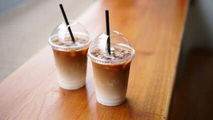 Two refreshing iced coffees with milk and coffee layers in clear plastic cups