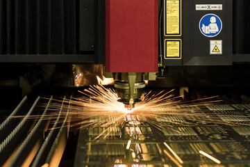 CNC laser cutting metal sheet with bright sparkle in factory.