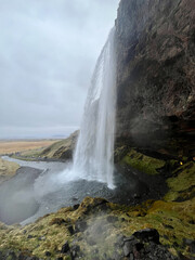 Side view of Seljalandsfoss waterfall in Iceland cascading down rugged cliff face under grey sky