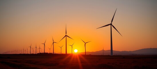 Obraz premium Beautiful Sunset Over Wind Turbines in an Open Landscape with Vibrant Orange and Yellow Sky Illustrating Renewable Energy and Nature Harmony