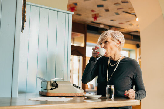 Senior writer drinking coffee and using typewriter in cafe