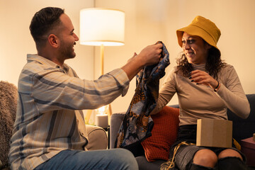 Happy couple exchanging gifts on sofa at home: giving clothes as a present