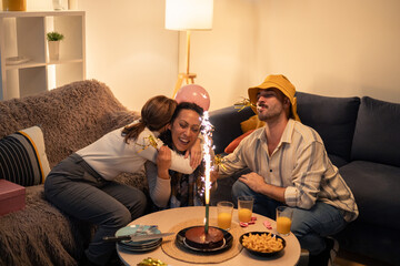Friends celebrating birthday at home with cake and sparklers