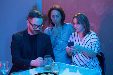 Friends using smartphones together at restaurant table in blue and pink light