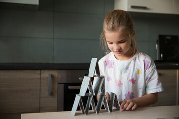 A little girl builds a house of cards on a table. Kidult gaming. Children's creativity.