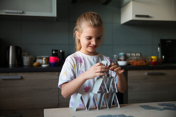 A little girl builds a house of cards on a table. Kidult gaming. Children's creativity.