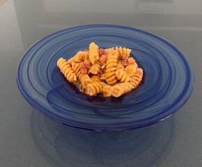 Closeup image of a plate of fusilli pasta with a Calabrese pesto sauce topped with crispy bacon and served in a blue glass bowl 