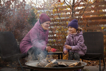 family mom and daughter is eight years oldl roasts marshmallows on an autumn day near a country house.  Family leisure with kids at autumn.