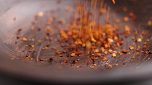 Crushed red cayenne pepper seasoning falling into wooden bowl in slow motion