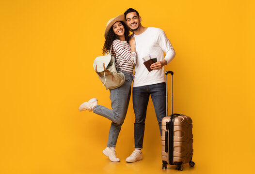 Portrait Of Happy Young Arab Spouses Ready For Vacation, Cheerful Middle Eastern Couple Standing With Suitcase, Pasports And Travel Tickets Over Yellow Background In Studio, Full Length, Copy Space
