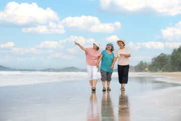 Senior women relaxing and walking hand in hand on beach. Asian mature female retired on vacation in...