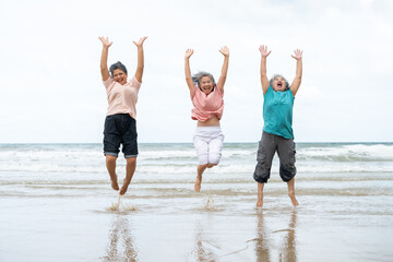 Happy senior women jump into the air with arms raised on beach. Asian mature female retired on...