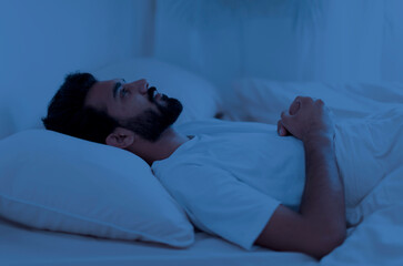 Awake sleepless upset indian man lying in bed alone at night, staring at ceiling, cant sleep, feeling lonely, suffering from depression or anxiety, experiencing difficulties with sleeping