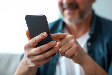Unrecognizable matured man using modern mobile phone, copy space, cropped, selective focus on smartphone. Modern technologies and mobile applications in elderly people daily routine concept