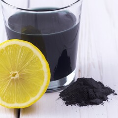 Charcoal lemonade detox drink in a clear glass, garnished with fresh lemon slice, accompanied by activated charcoal powder on a wooden surface, promoting health and wellness benefits