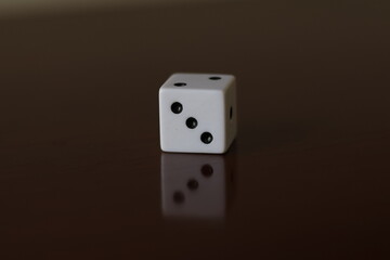 Una toma de cerca  de uno o varios dados blancos para juego en una mesa de color marrón oscuro como fondo