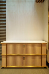 Elegant fluted wood cabinet with a white marble top and brass details against a blank wall. Modern, minimalist furniture with copy space above. © Okta
