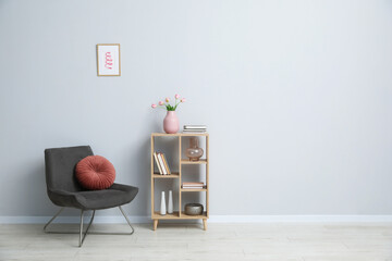 Naklejka na ściany i meble Comfortable armchair and wooden rack with different decor near light gray wall indoors. Space for text