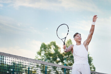 Young man playing tennis at court on sunny day, low angle view. Space for text