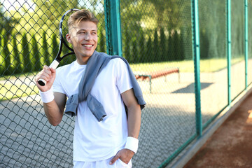 Young man with racket at tennis court. Space for text