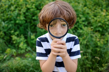 Cute little boy looking through magnifying glass in nature