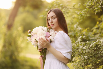 Fototapeta premium Beautiful woman with bouquet of peonies in park