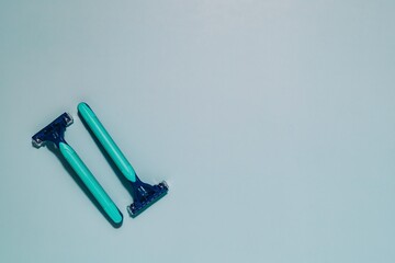 Two identical blue and green manual razors neatly arranged on a calm blue background with copy space. Represents personal grooming, hygiene, and a shaving set.
