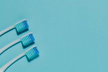 Three white toothbrushes with blue bristles, diagonally arranged on soothing blue. Highlights oral hygiene, dental care, family health, and bathroom essentials.