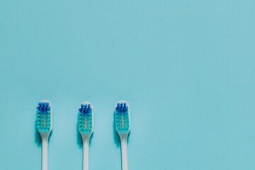 Heads of three white toothbrushes with blue bristles at the bottom of serene blue. Emphasizes oral hygiene, dental care, daily routines, and family health.