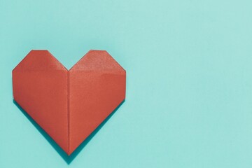 Perfectly folded red origami heart on clean blue with ample copy space. Beautifully conveys love, care, creativity, handmade gifts, and heartfelt expression.