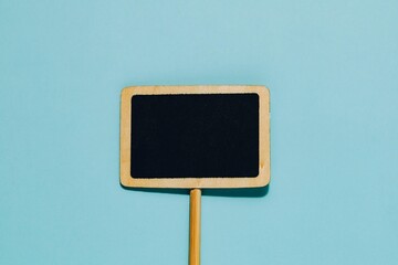 Blank wooden framed chalkboard sign on a stick, centered on a clean blue background. Ideal for messages, promotions, announcements, customization, placeholders.