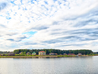 Calm lake view with colorful houses amid lush green trees under a cloudy sky in a serene rural setting